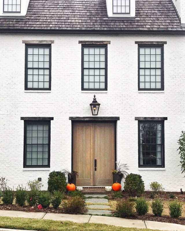 White brick home with black trim around the windows. Pumpkins on the front steps